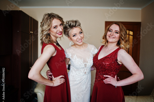Blonde bride with bridesmaids wear on red dress at room on morning wedding day.