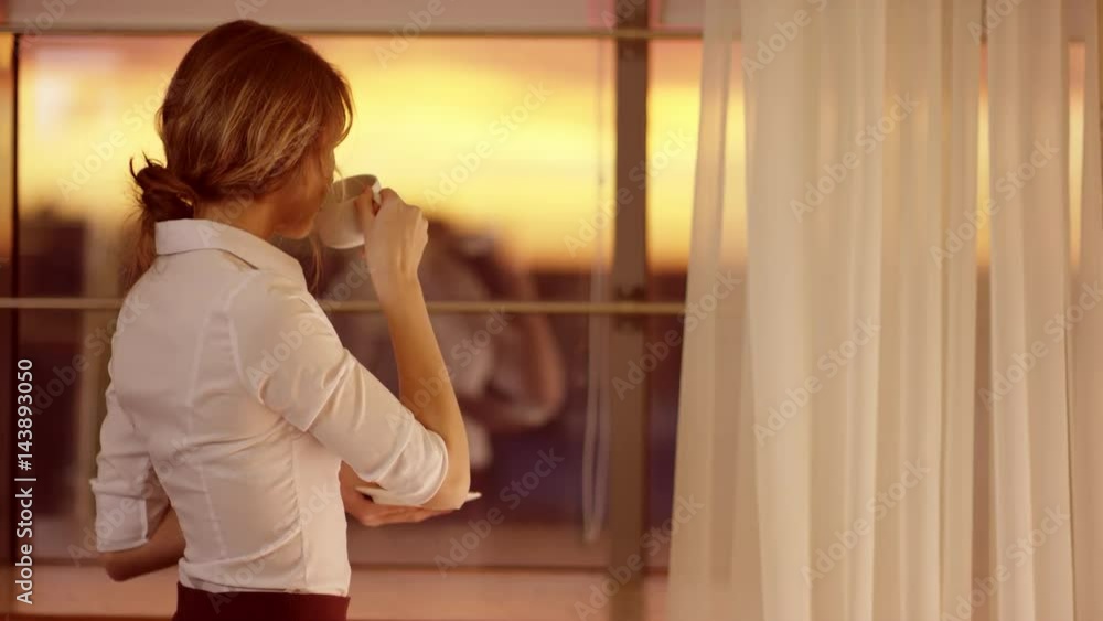 Young woman stands in front of the window and drinks a cup of tea or coffee Young woman stands in front of the window and drinks a cup of tea or coffee