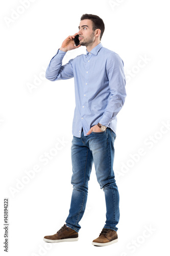 Successful young businessman talking on the phone looking away. Full body length portrait isolated over white background.