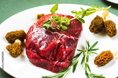 Raw beefsteak on plate, herb, mushroom.