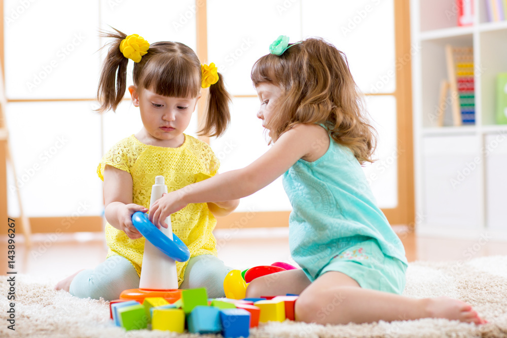 Children playing together. Toddler kid and baby play with blocks. Educational toys for preschool and kindergarten child. Little girls build pyramid toys at home or daycare. Stock Foto Adobe Stock