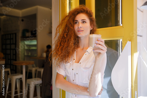 Cute redhead woman with long hair holding cup of coffee