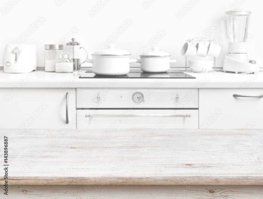 Wooden table in front of blurred white kitchen bench interior Wooden table in front of blurred white kitchen bench interior