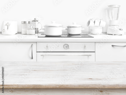 Wooden table in front of blurred white kitchen bench interior