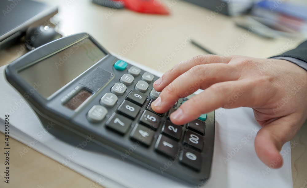 A young man is calculating on a calculator. He needs to see how much money he earned this month. A young man is calculating on a calculator. He needs to see how much money he earned this month.