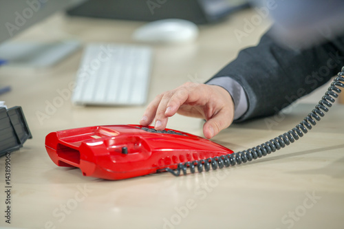 A young businessman is dialing a number on the office telephone. He is making an important telephone call.