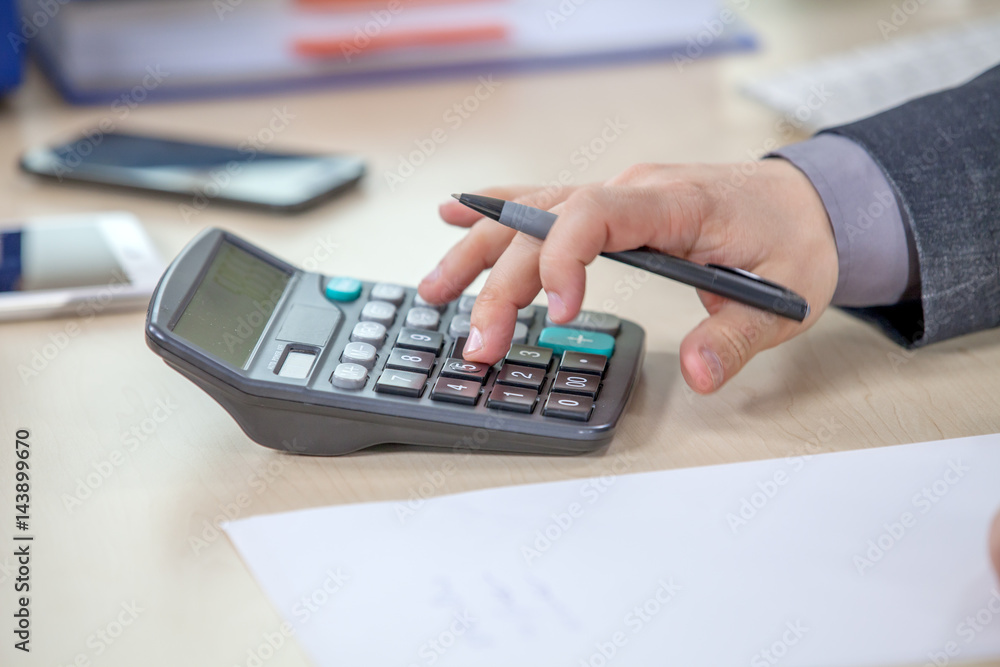 A young businessman is typing something on the calculator. He is also holding a pencil in his hand. A young businessman is typing something on the calculator. He is also holding a pencil in his hand.