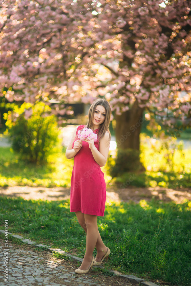 Beautiful girl posing to the photographer against the background of blooming pink trees. Spring. Sakura. Beautiful girl posing to the photographer against the background of blooming pink trees. Spring. Sakura.