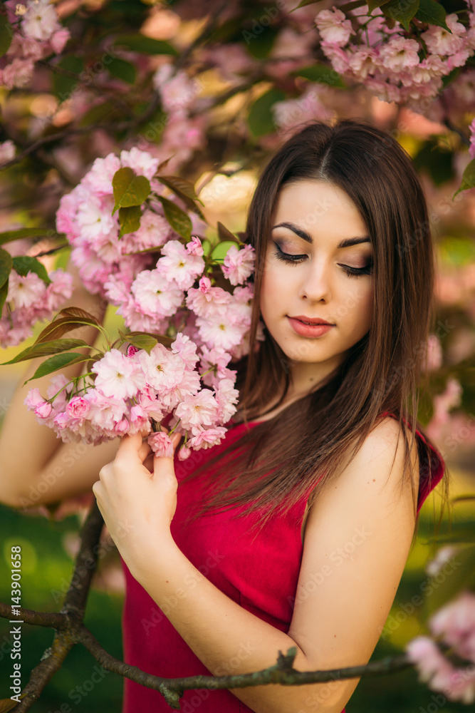 Beautiful girl posing to the photographer against the background of blooming pink trees. Spring. Sakura. Beautiful girl posing to the photographer against the background of blooming pink trees. Spring. Sakura.