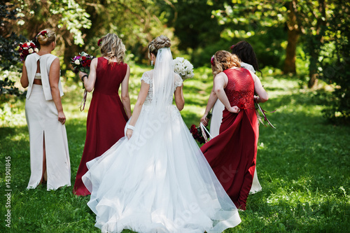 Gorgeous blonde bride with four bridesmaids at red and beige dresses outdoor.