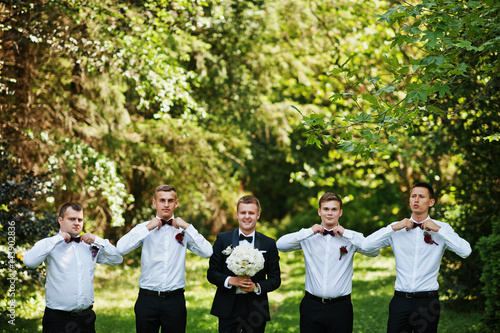 Fashionable groom with four best mans at bow ties outdoor.