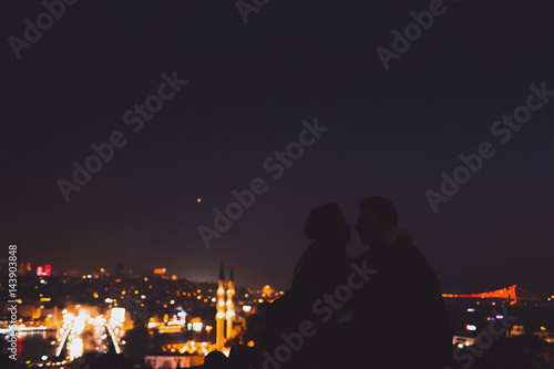 Couple on Valide Han roof. Illuminated lights of night Istanbul view