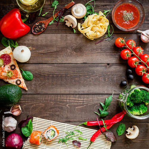 Food frame of vegetables, pizza, sushi rolls, tomato, pasta, olives and sauce on wooden background. Flat lay. Top view