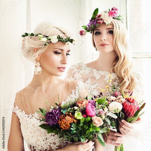 Two Beautiful Blonde Women Fiancee. Fashion Model with Flower Arrangement  Flower Wreath  Wedding Hairstyle and Makeup