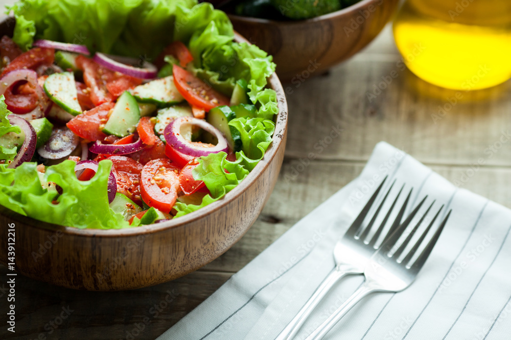 Rustic salad of fresh tomatoes, cucumbers, red onions and lettuce, dressed with olive oil and ground pepper in a wooden bowl. Top view Rustic salad of fresh tomatoes, cucumbers, red onions and lettuce, dressed with olive oil and ground pepper in a wooden bowl. Top view