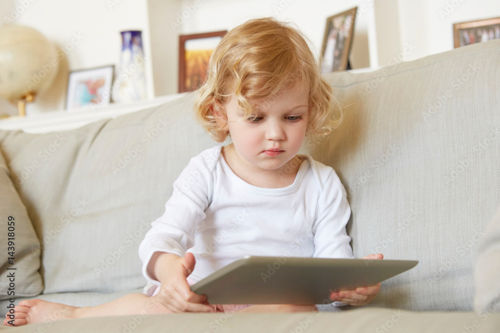 Female toddler sitting on sofa using digital tablet Female toddler sitting on sofa using digital tablet