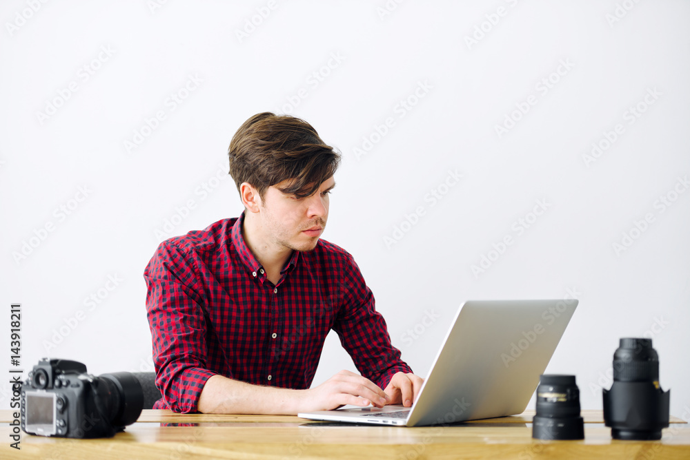 Man is working on a laptop in the office. On the table, a SLR camera and lenses Man is working on a laptop in the office. On the table, a SLR camera and lenses