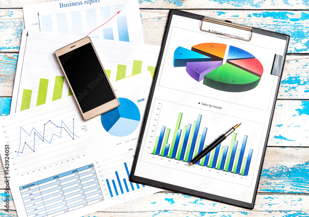 Business graphs with smartphone on the wooden table. Business concept. Business graphs with smartphone on the wooden table. Business concept.