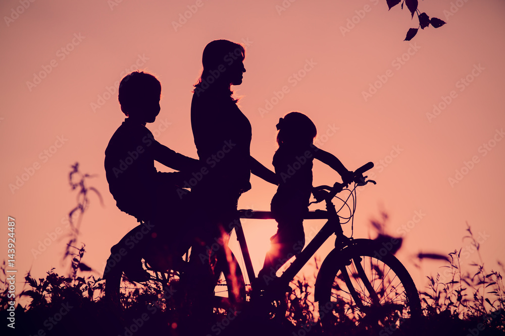 mother with son and daughter riding bike at sunset