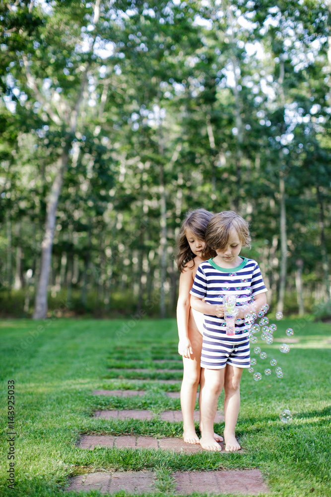 Girl and boy watching bubbles from toy bubble maker in garden Girl and boy watching bubbles from toy bubble maker in garden