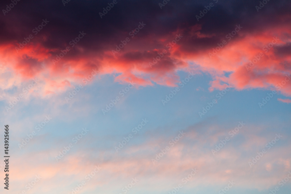 Beautiful sky background with dark blue, red stormy cloud at the top and light blue, pink sky at the bottom. Contrast pattern at sunset.