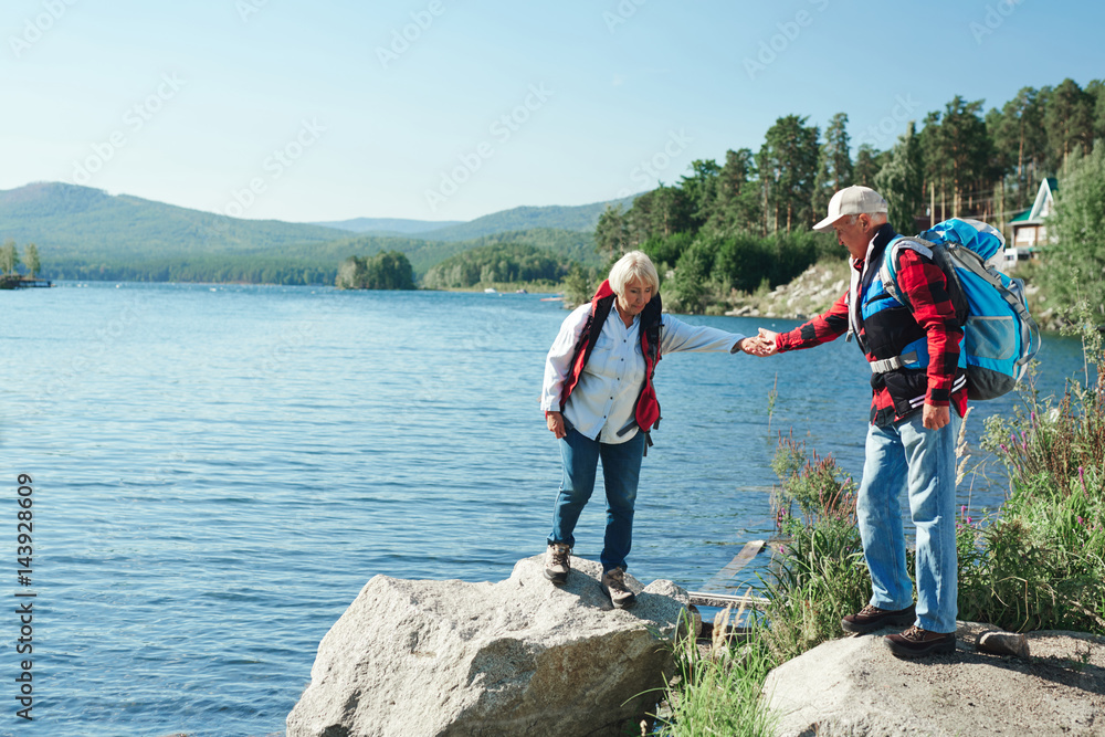 Mature man helping his wife walk on stone during trip in the country