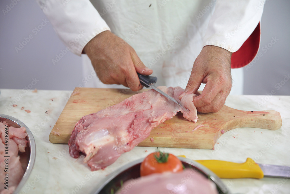 A chef is cutting the skin off the turkey meat. He is doing this on a wooden board.