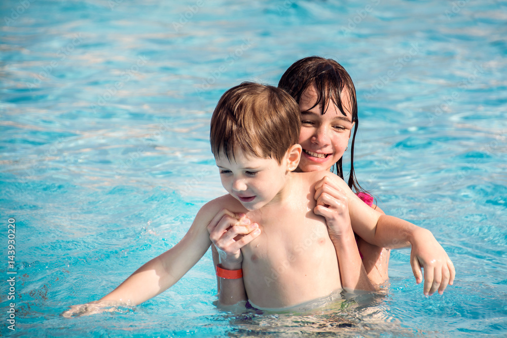 The elder sister holds a younger brother in the children's pool with blue water