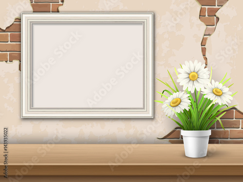 Vintage background with brick wall, wooden table, picture frame and flower in pot.