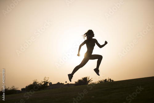 Dark silhouette of an athletic woman leaping as she jogs with a sunset in the background 