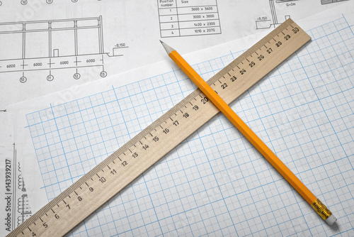 Open blueprints on wooden table background with a pencil and a ruler lying beside.