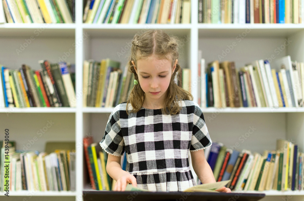 Pretty little girl reading a book in library. Pretty little girl reading a book in library.