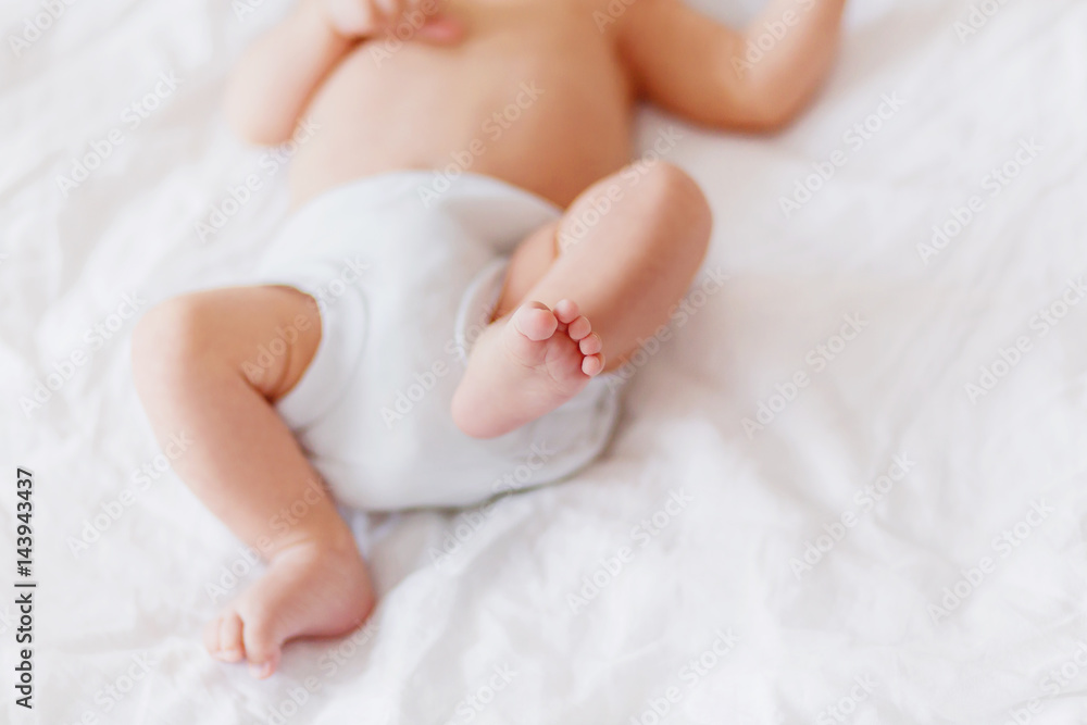 Baby's feet. Little child wearing white bodysuit and diaper. Cozy morning bedtime at home. Baby's feet. Little child wearing white bodysuit and diaper. Cozy morning bedtime at home.