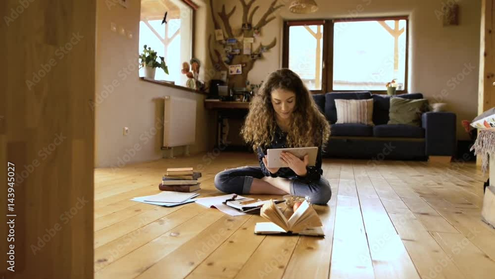 Teenage girl sitting on the floor holding tablet, studying