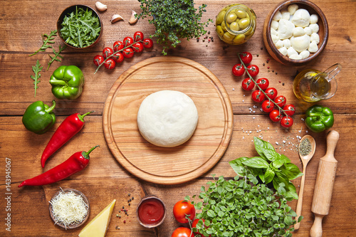 Italian food cuisine background. Pizza cooking ingredients: dough, mozzarella, tomatoes, basil, olive oil, cheese, sauce, spices, regano parmesan pepper herbs served on rustic wooden table
