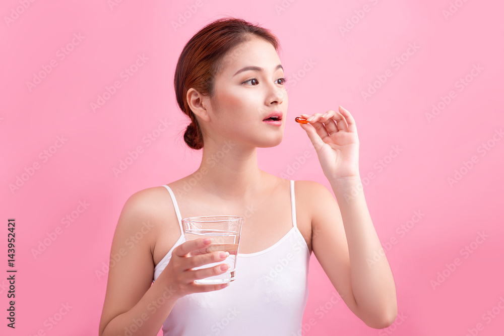 Young asian beauty young woman eating pills and drinking water on pink background. Young asian beauty young woman eating pills and drinking water on pink background.
