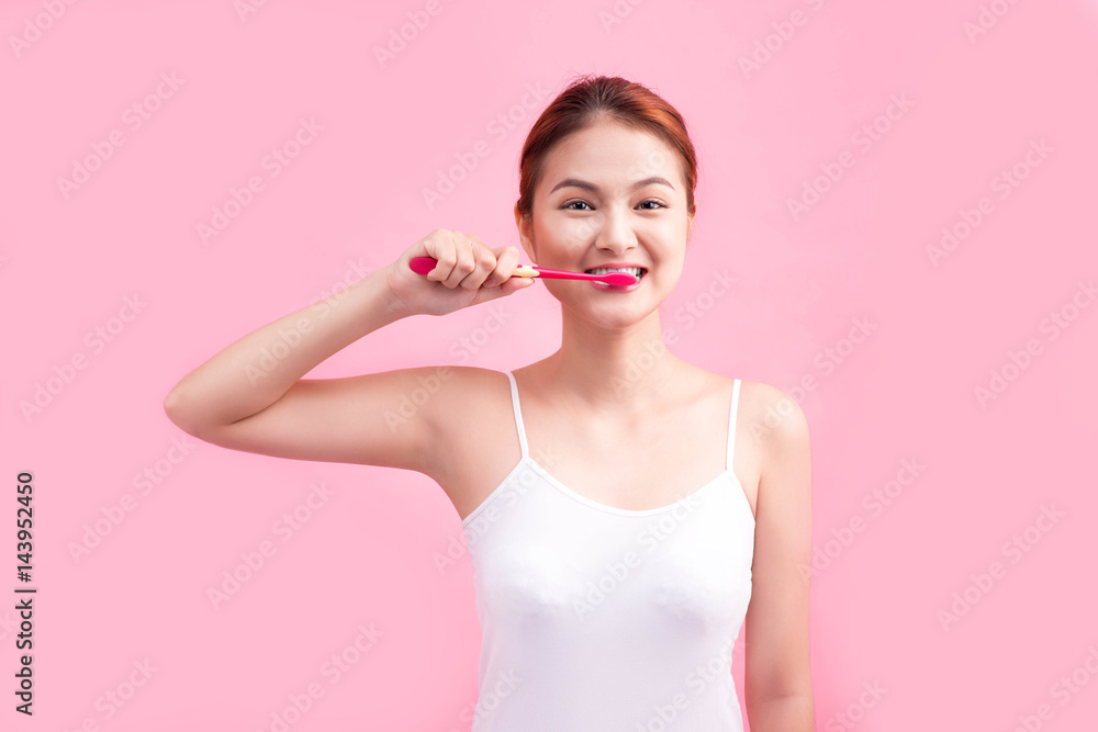 Smiling young woman with healthy teeth holding a tooth brush over pink background.