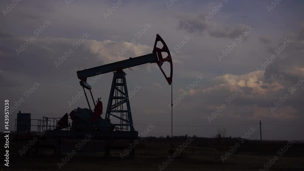 Silhouette of a running oil pump. Cloudy sky Silhouette of a running oil pump. Cloudy sky