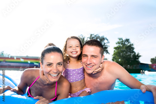 Mother, father and daughter in swimming pool. Sunny summer.