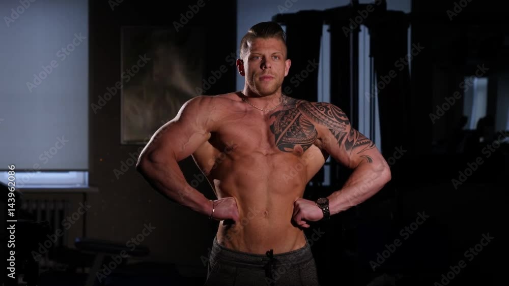 Young bodybuilder with a bare torso posing in a gym. 60 to 24fps 4K Young bodybuilder with a bare torso posing in a gym. 60 to 24fps 4K