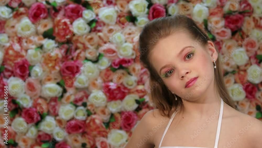 Air Kiss Baby. Close up little girl in white dress posing against a background of a flower wall in the studio Air Kiss Baby. Close up little girl in white dress posing against a background of a flower wall in the studio