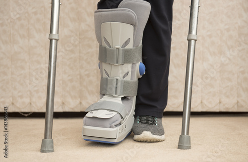 Unrecognisable woman wearing a medical orthopaedic boot with crutches Fototapeta