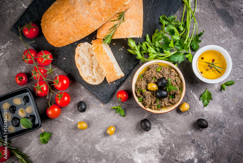 Homemade traditional Italian appetizer tapenade from green and black olives, white ciabatta, fragrant herbs and oil, fresh tomatoes. On a concrete gray table, copy space top view © ricka_kinamoto