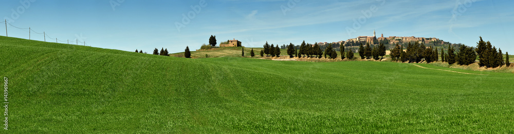 PIENZA, TUSCANY / ITALY - MAR 31, 2017: beautiful landscape, with green rolling hills and tuscan cypress trees with Medieval Village of Pienza on background. Located in Siena countryside. Italy.