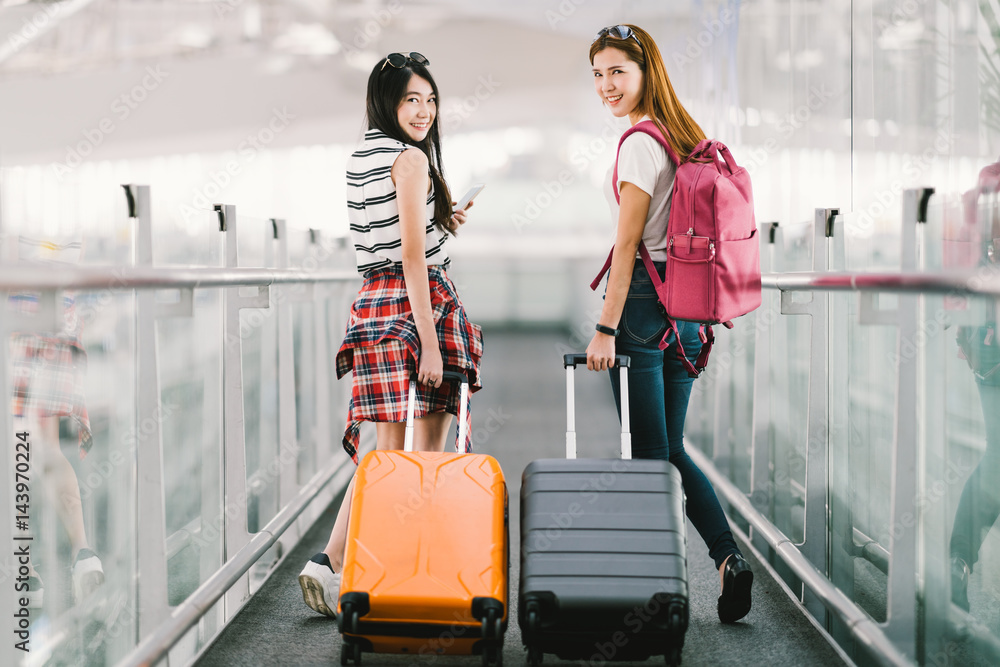 Two happy Asian girls traveling abroad together, carrying suitcase luggage  in airport. Air travel or holiday vacation concept Photos | Adobe Stock