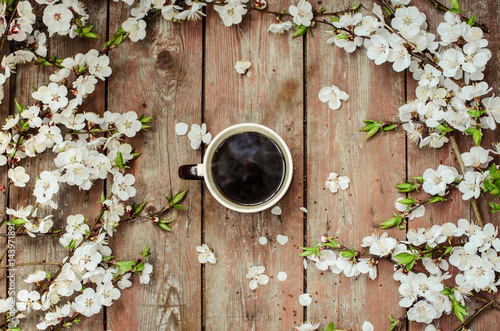 Cup of hot black coffee in female hands on a wooden vintage desk with spring white flowers apricorn. The concept of coffee on a spring day.