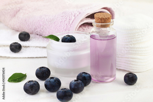 Berry extract cosmetic products. Lilac facial gel in glass bottle, blueberries, cream and towels. 
