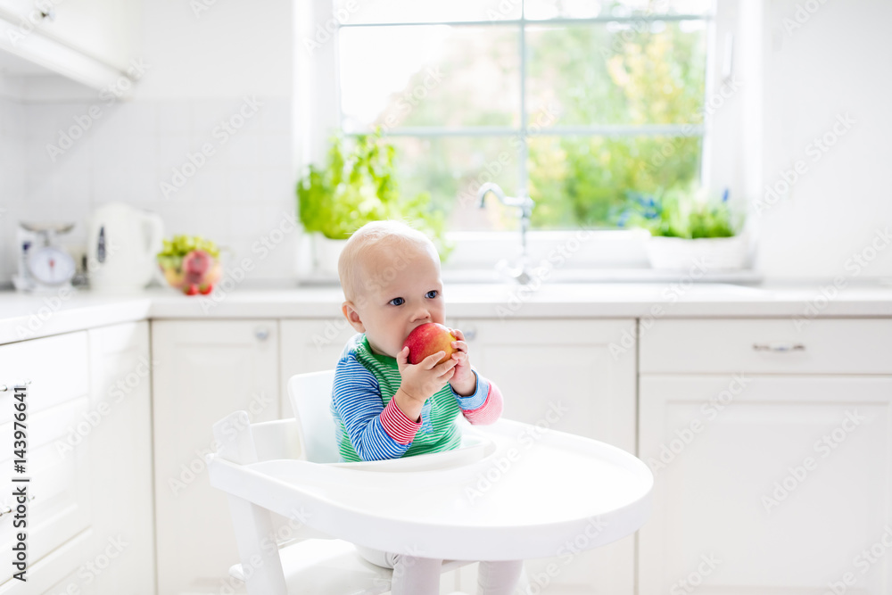 Baby boy eating apple in white kitchen at home Baby boy eating apple in white kitchen at home