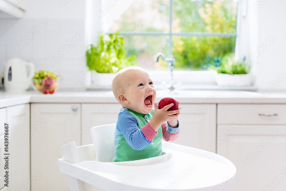 Baby boy eating apple in white kitchen at home Baby boy eating apple in white kitchen at home