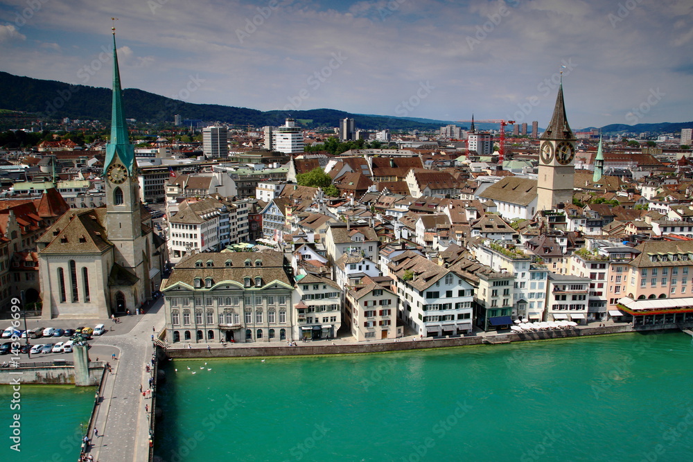 Fototapeta premium Szeroki kąt panoramy centrum Zurychu: rzeka Limmat, dachy starego miasta, kościół Fraumunster i kościół św.Piotra z największym zegarem w Europie w słoneczny dzień, z katedry Grossmunster w Szwajcarii